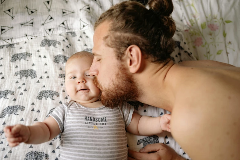 a man laying on top of a bed next to a baby, pexels contest winner, happening, groomed beard, australian, thumbnail, up close picture