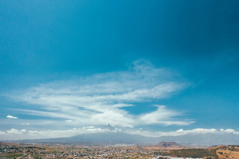 a view of a city from the top of a hill, by Alejandro Obregón, pexels contest winner, hurufiyya, blue sky and white clouds, volcano landscape, slightly pixelated, midday photograph