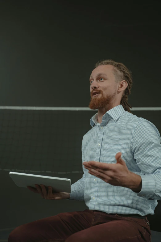 a man sitting on a chair holding a tablet, a hologram, unsplash, volley court background, braided beard redhead dreadlocks, standing in class, low quality footage