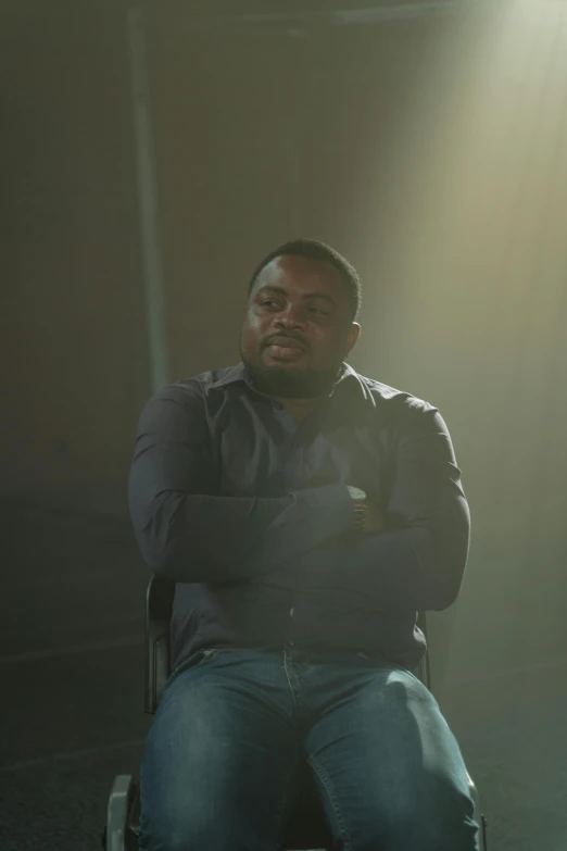 a man sitting in a chair in a dark room, by Stokely Webster, 3 actors on stage, david uzochukwu, episode still, timothy rees