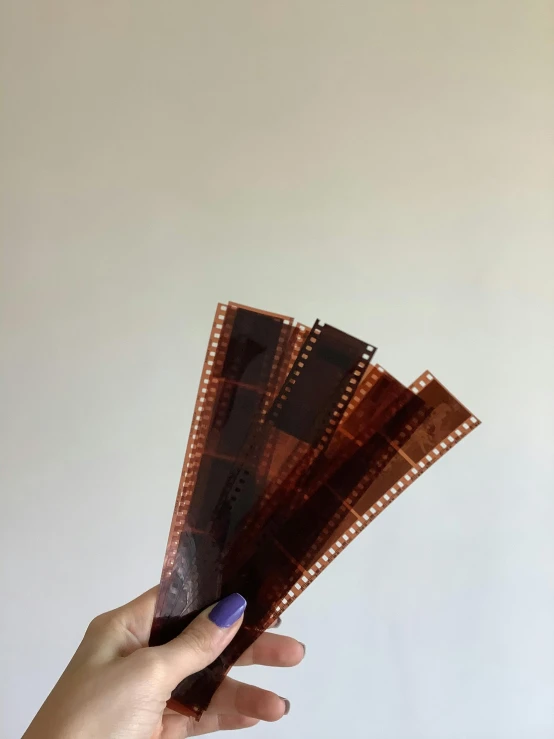 a person holding a film strip in their hand, by Aileen Eagleton, video art, hand carved brown resin, vsco film grain, chocolate, technicolour film