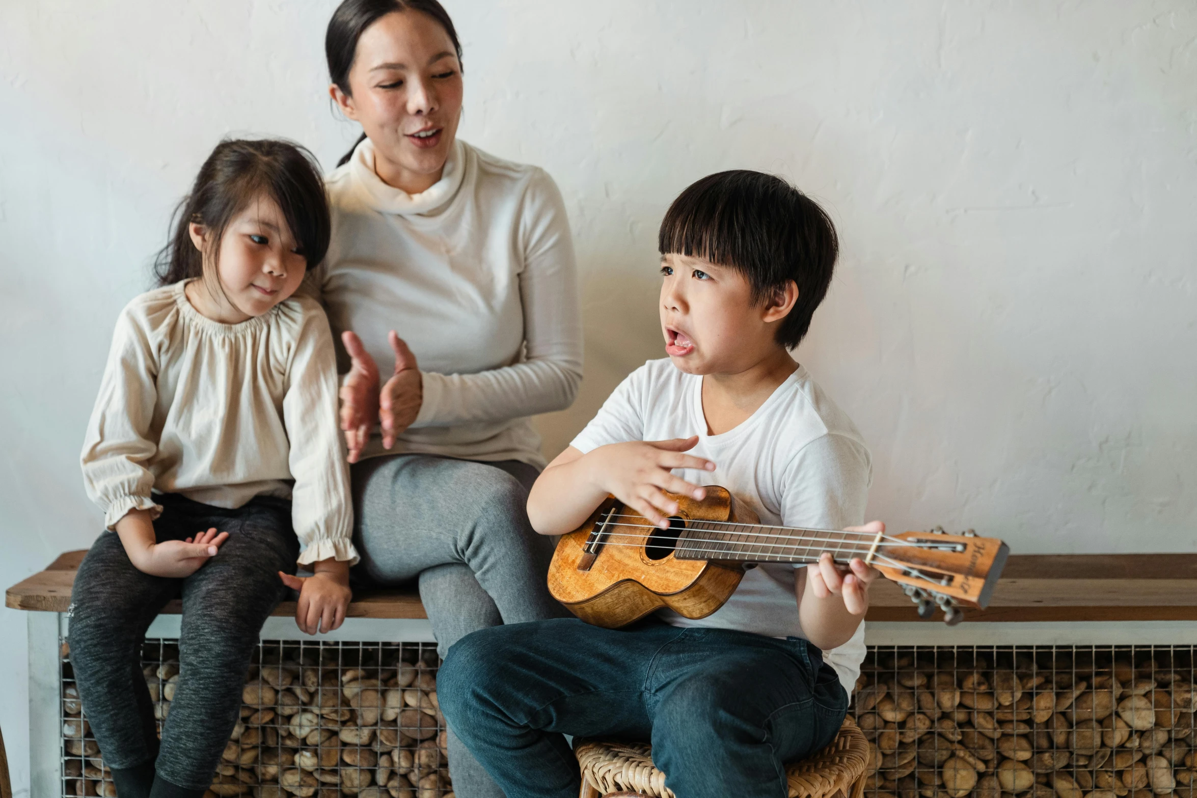 a woman and two children sitting on a bench with a guitar, inspired by Tani Bunchō, pexels contest winner, mingei, singing, in house, nanae kawahara, thumbnail