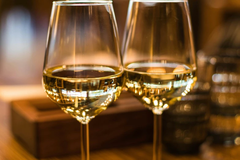 two glasses of wine sitting on a table, pexels contest winner, white and gold color scheme, thumbnail, warm glow, engineered