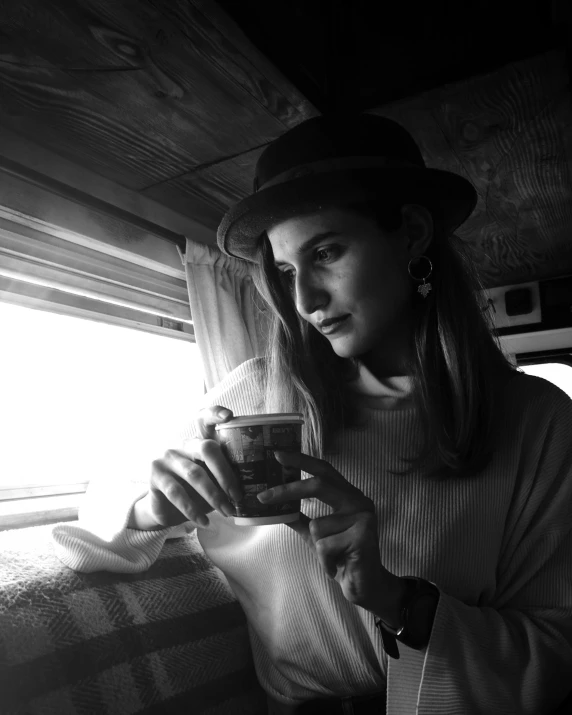 a black and white photo of a woman holding a cup, inspired by Vivian Maier, unsplash, noir detective and a fedora, in a cabin, lana del rey, artem chebokha