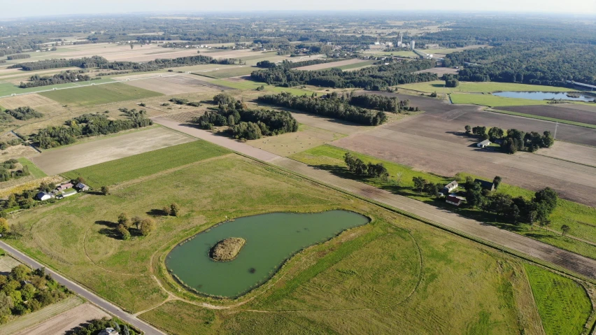 an aerial view of a farm with a pond, by Daarken, pixabay, land art, looking towards the horizon, 15081959 21121991 01012000 4k, in the center midground, rutkowskyi