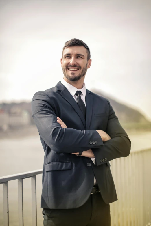 a man in a suit standing with his arms crossed, a colorized photo, pexels contest winner, renaissance, smiling :: attractive, on a bridge, strong masculine features, professional profile picture