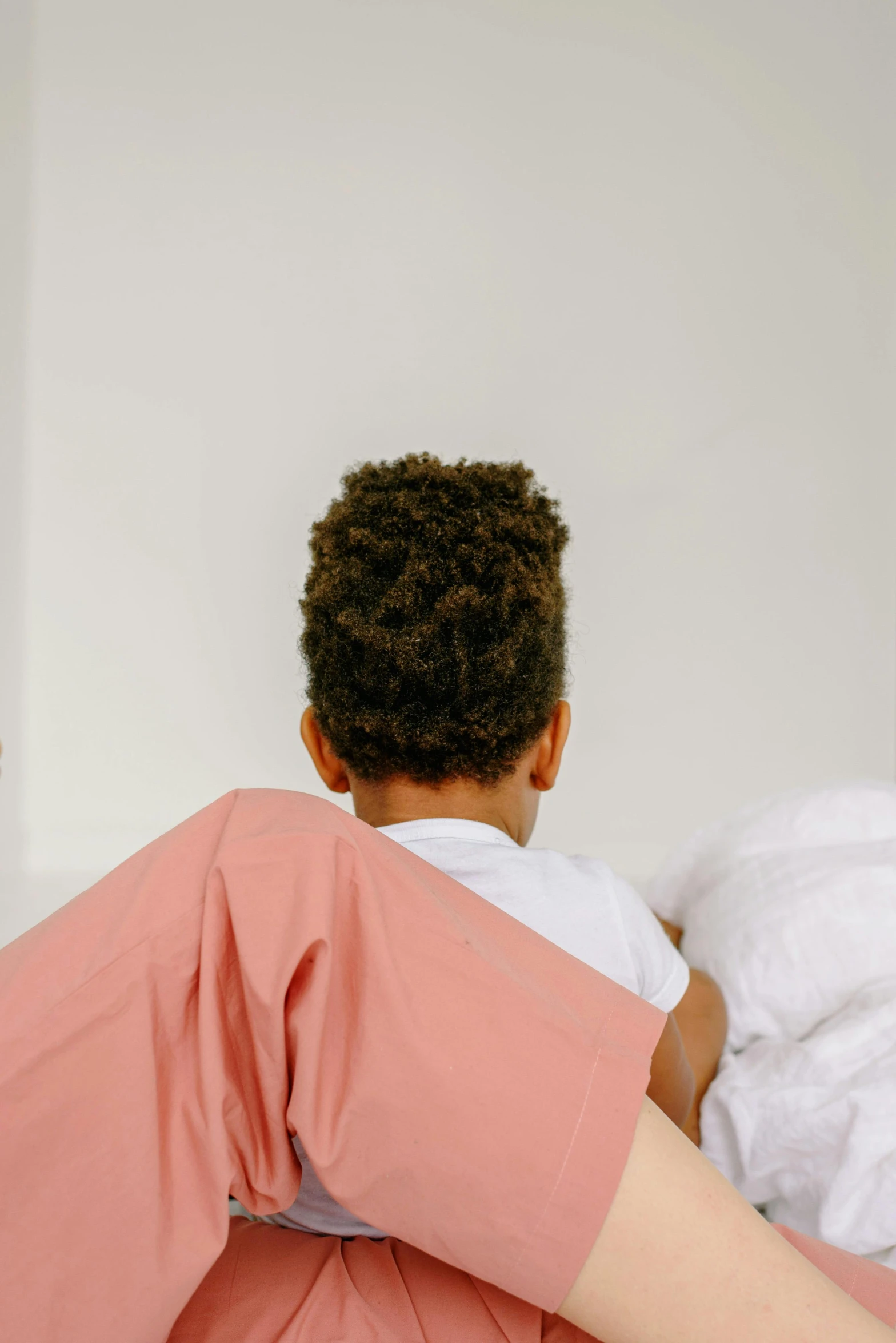 a woman sitting on top of a bed next to a man, by Everett Warner, pexels contest winner, bright red cape on her back, healthcare worker, african american young woman, back view. nuri iyem