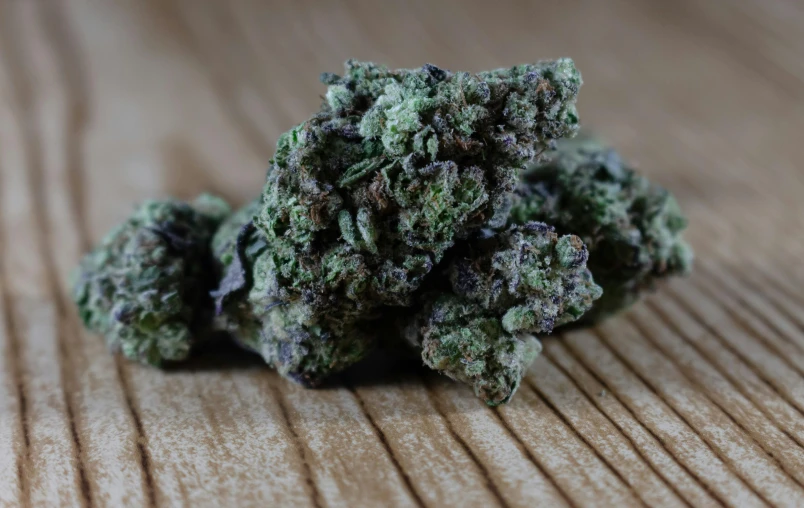 a pile of purple marijuana sitting on top of a wooden table, a portrait, unsplash, detailed product image, lush greens, from the side, high quality product image”