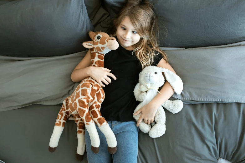 a little girl laying on a bed holding a stuffed giraffe, inspired by Sarah Lucas, pexels contest winner, the woman holds more toys, brown, hugging each other, fullbody view