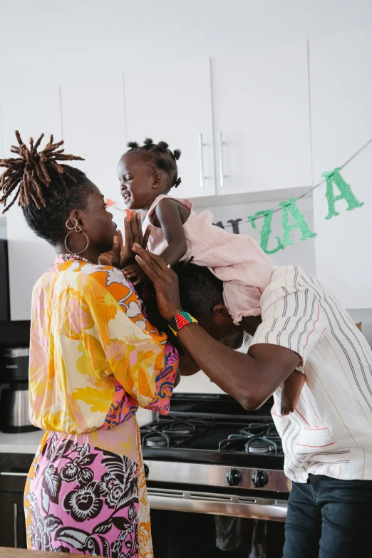 a woman holding a baby in a kitchen, an album cover, inspired by Ras Akyem, pexels contest winner, dada, at a birthday party, dreadlock breed hair, portrait of family of three, lupita nyong'o