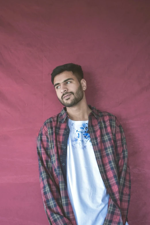 a man standing in front of a red wall, an album cover, by Adam Dario Keel, hurufiyya, wearing a tie-dye t-shirt, wearing a flannel shirt, full frame image, reza afshar