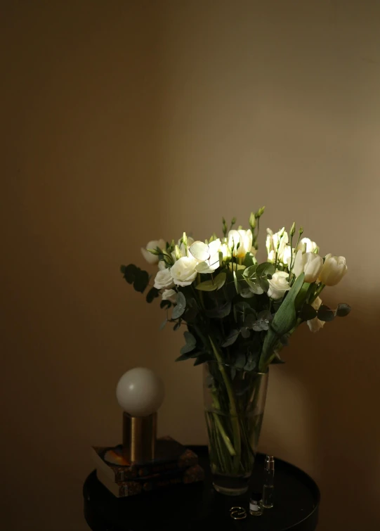 a vase filled with white flowers sitting on top of a table, inspired by Elsa Bleda, romanticism, night light, roses and tulips, hotel room, soft light - n 9