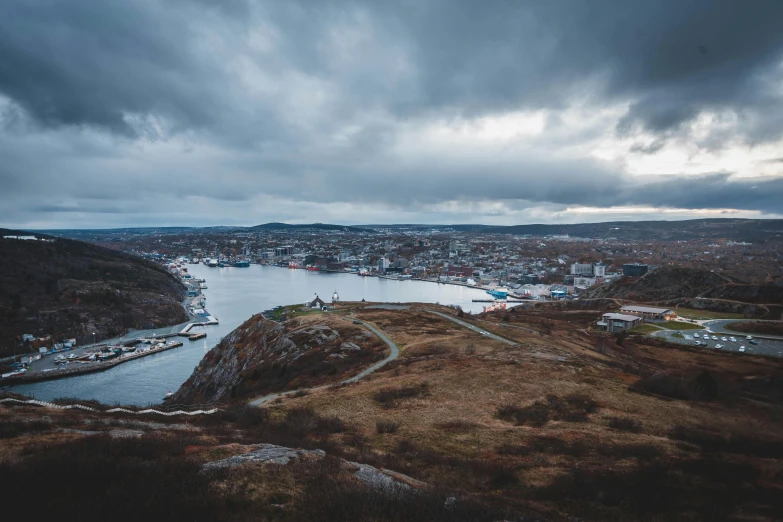 a large body of water sitting next to a lush green hillside, a tilt shift photo, by Jesper Knudsen, pexels contest winner, happening, harbour, under a dark cloudy sky, stålenhag, a cozy