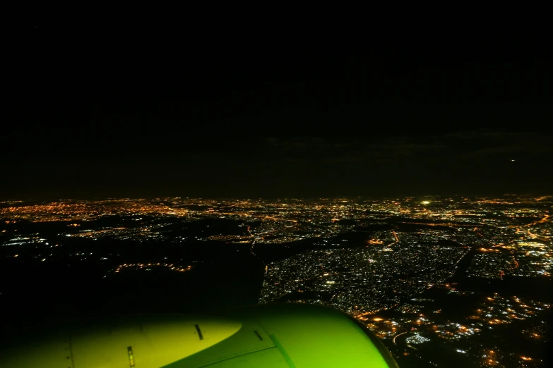 an airplane flying over a city at night, a picture, hurufiyya, ambient green light, são paulo, sitting down, a green