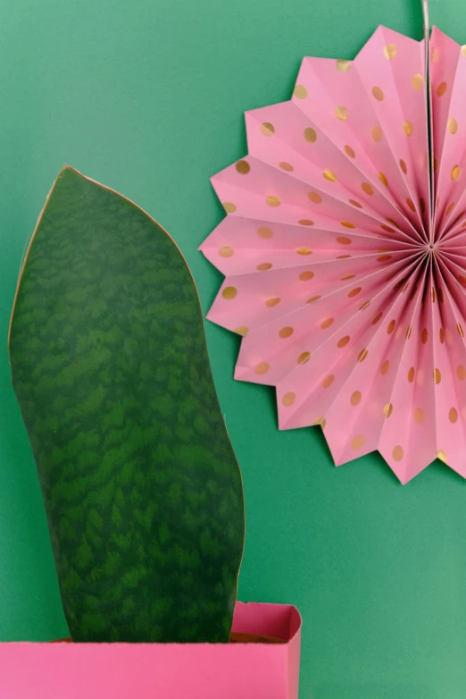 a paper flower hanging on a wall next to a potted plant, by Rachel Reckitt, tropical leaves, polka dot tables, detailed product shot, pink and gold