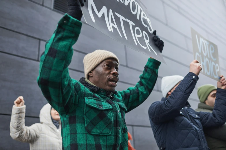 a man holding up a sign in front of a building, by Jakob Emanuel Handmann, pexels contest winner, black arts movement, hands raised in the air, wintermute, actor, lil uzi vert