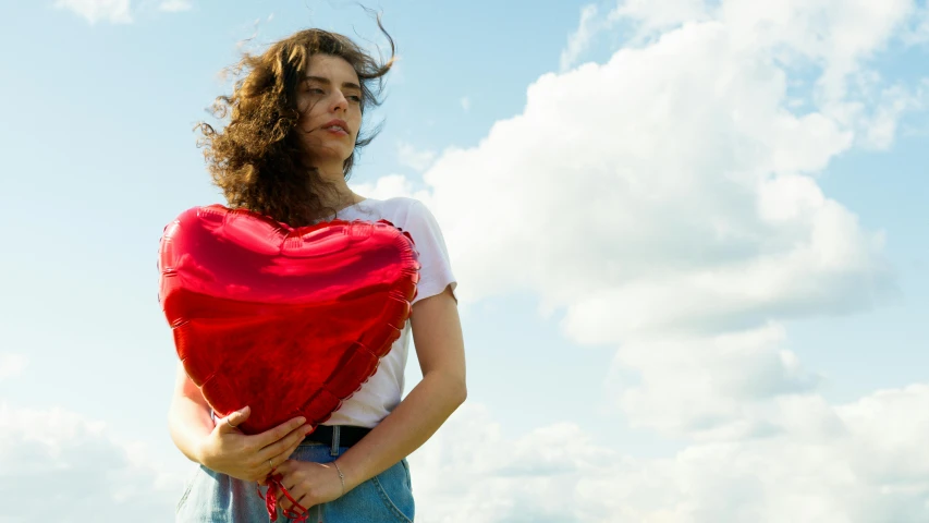 a woman holding a red heart shaped balloon, an album cover, by Julia Pishtar, pexels contest winner, lorde, blue sky, hozier, rebecca sugar