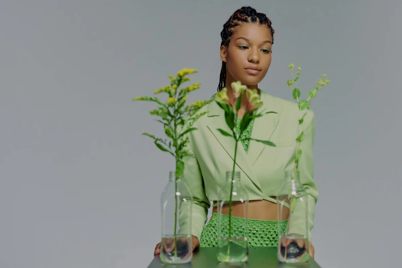 a woman holding a vase with flowers in it, an album cover, trending on pexels, wearing green clothing, ashteroth, stood in a lab, sustainable materials