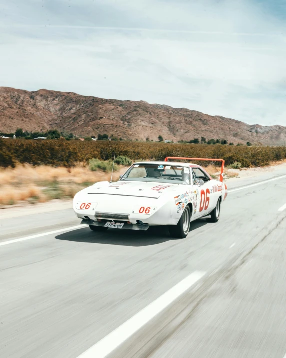 a white car driving down a road with mountains in the background, a portrait, unsplash, retrofuturism, nascar, 7 0 s photo, ultra 4 k, california