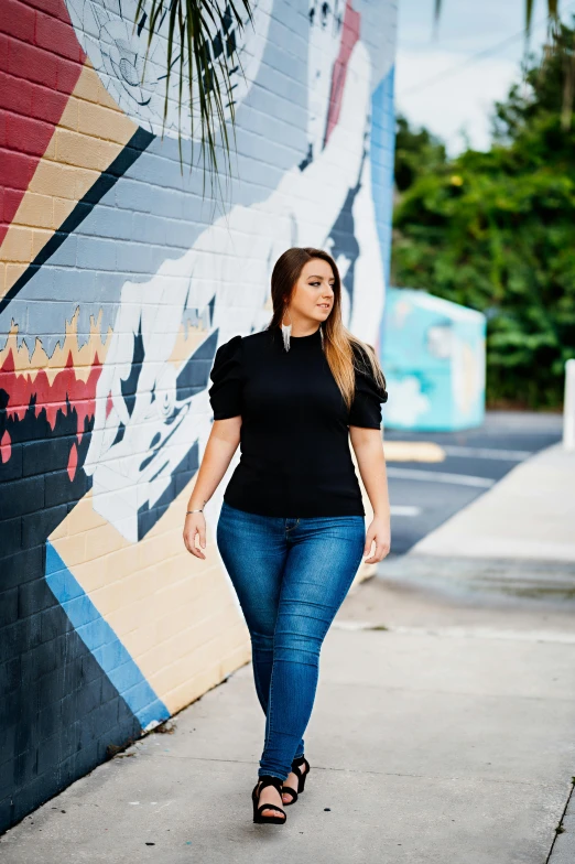 a woman walking down a sidewalk next to a wall, by Briana Mora, wearing a dark shirt and jeans, curves!!, curated collections, puff sleeves