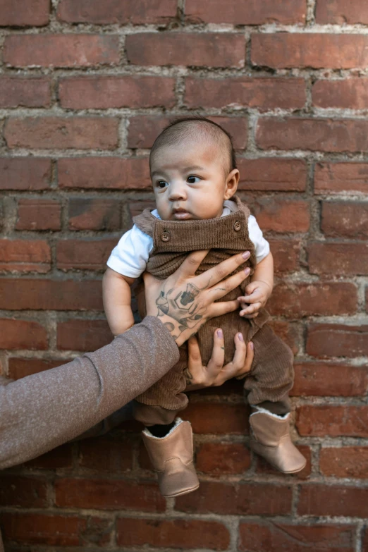 a woman holding a baby in front of a brick wall, by Nina Hamnett, trending on unsplash, brown suit vest, wears brown boots, asian man, slide show