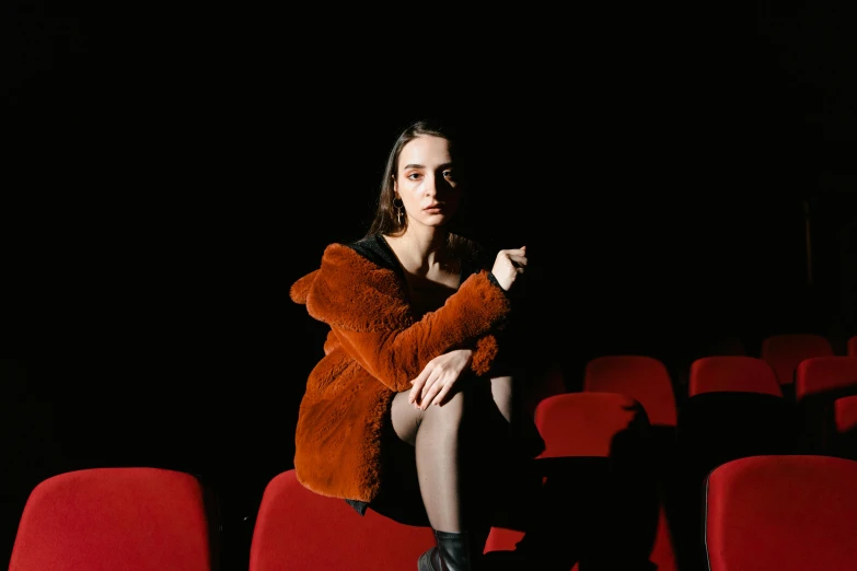 a woman sitting in a theater holding a teddy bear, an album cover, pexels contest winner, antipodeans, lilly collins, red leather short coat, black and orange coat, ( ( theatrical ) )