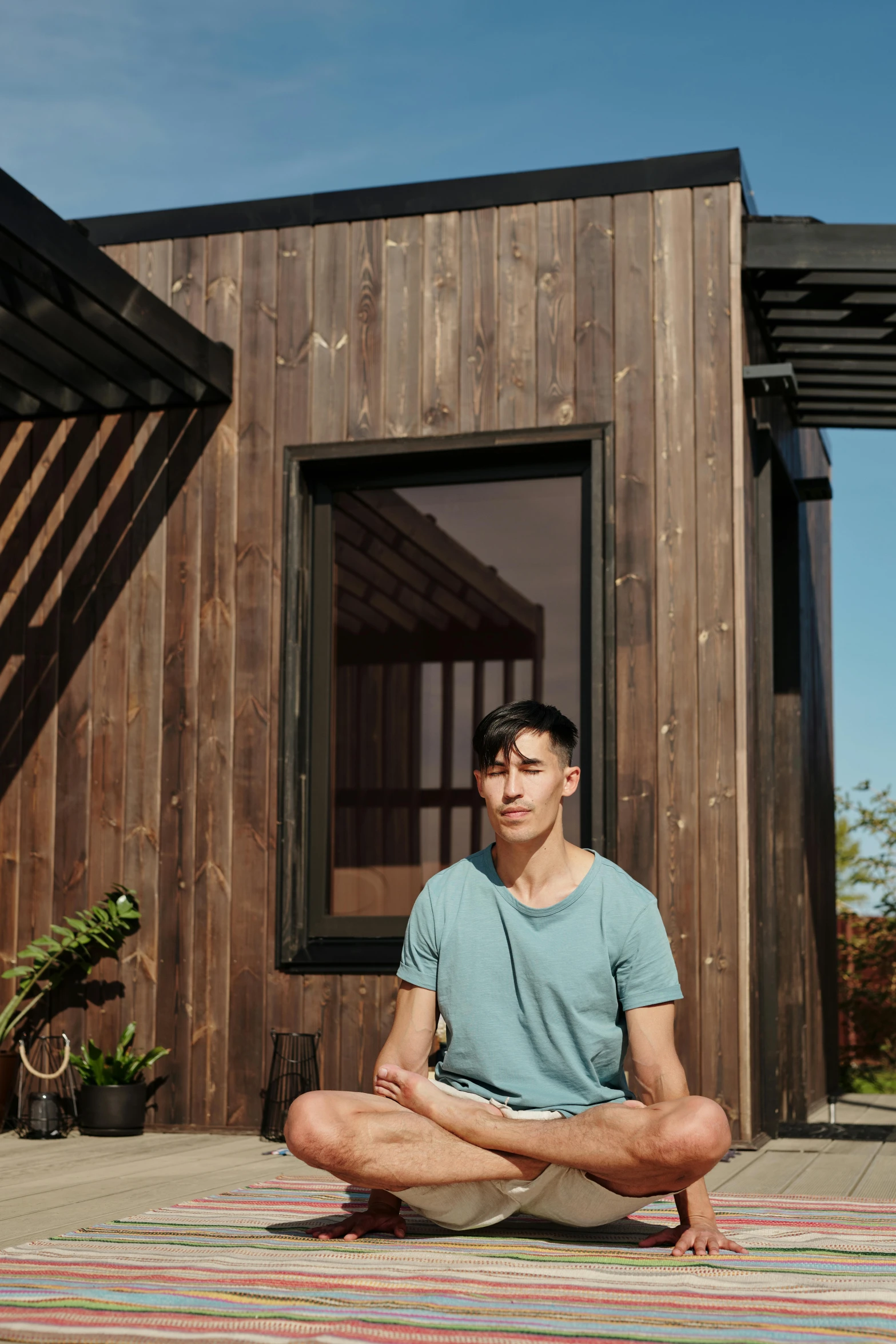 a man sitting on a rug in front of a house, a portrait, unsplash, conceptual art, health spa and meditation center, tiny house, handsome chad chin, open window ib background