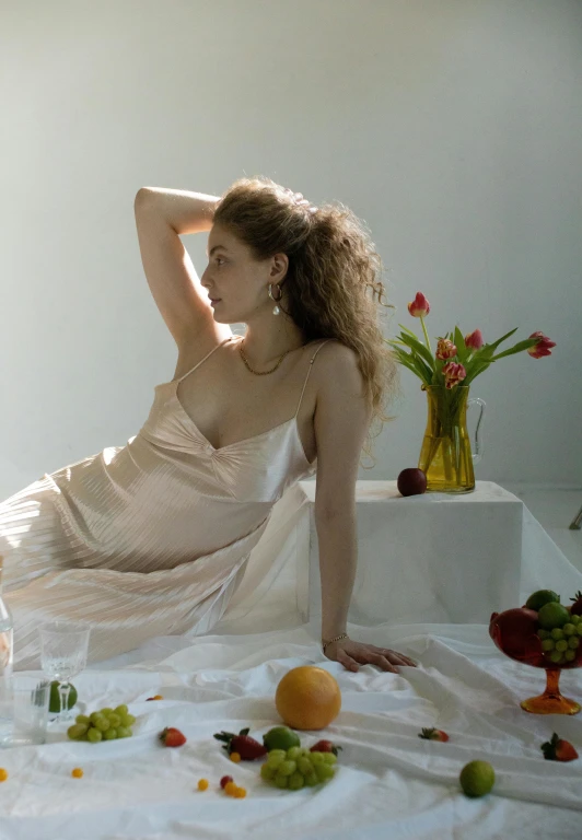 a woman in a white dress sitting on a bed, a still life, inspired by Anna Füssli, unsplash, renaissance, at a dinner table, translucent silky dress, in a style blend of botticelli, peach