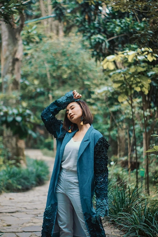 a woman standing on a path in a forest, an album cover, by Basuki Abdullah, unsplash, sumatraism, wearing a blue jacket, casual pose, cardigan, in garden