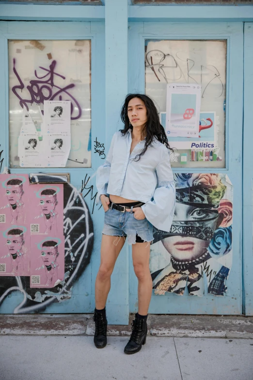 a woman standing in front of a blue door, pexels contest winner, graffiti, wearing denim short shorts, oona chaplin, li bingbing, wearing a light blue shirt