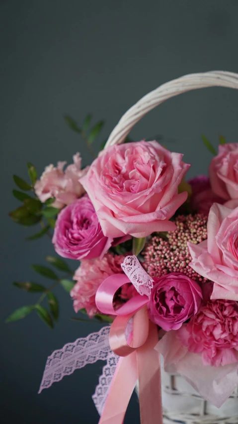 a basket filled with pink flowers on top of a table, on grey background, carefully crafted, close up details, feature