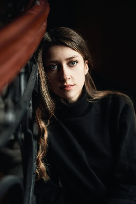 a woman sitting on a chair in a dark room, a character portrait, by Elizabeth Polunin, pexels contest winner, black turtleneck, natalia dyer, square, medium format. soft light