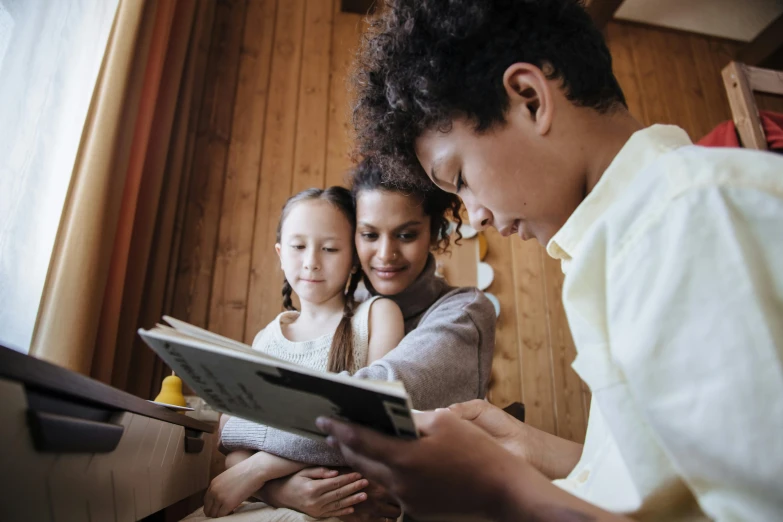 a couple of people that are looking at a book, a portrait, by Lee Loughridge, pexels, families playing, varying ethnicities, kids, a wooden