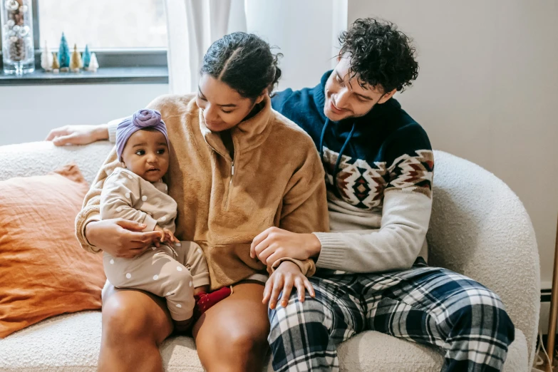 a man and woman sitting on a couch holding a baby, pexels contest winner, incoherents, diverse outfits, manuka, mixed race, cozy aesthetic