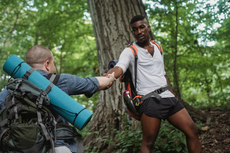 two men shaking hands in the woods, pexels contest winner, renaissance, man is with black skin, white shorts and hiking boots, meet the actor behind the scenes, a man wearing a backpack