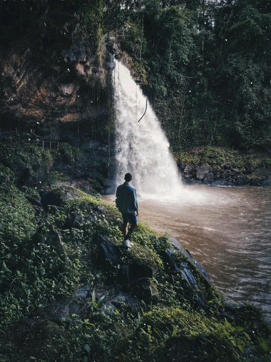 a man standing in front of a waterfall, inspired by Elsa Bleda, sumatraism, still from a nature documentary, trending on vsco, colombian, overlooking