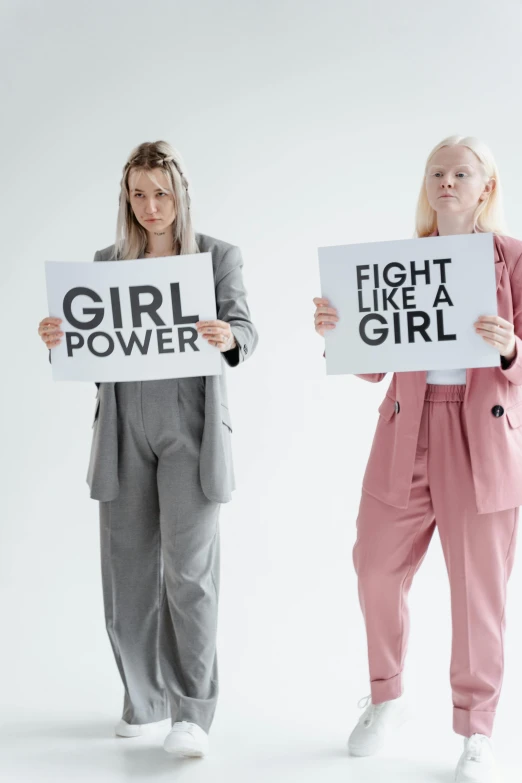 two women holding signs that say fight like a girl, trending on pexels, wearing a light - pink suit, on a gray background, elle fanning), androgynous person