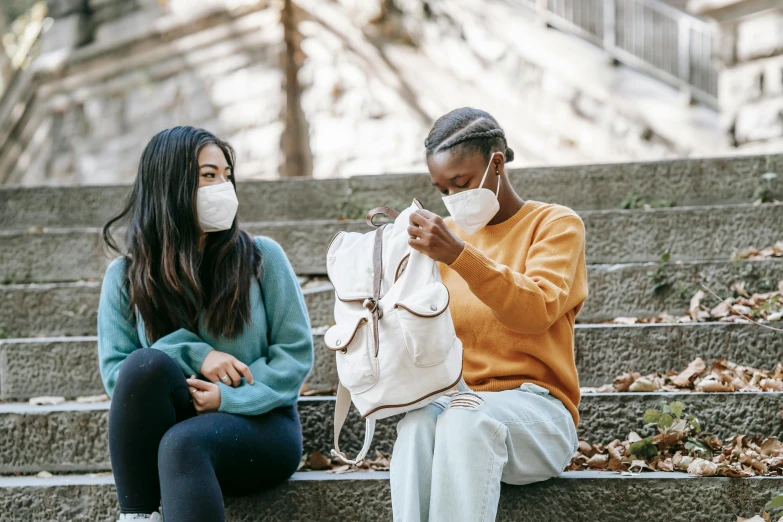 a couple of women sitting next to each other on some steps, trending on pexels, happening, bag - valve mask, student, with a covered face, as well as scratches