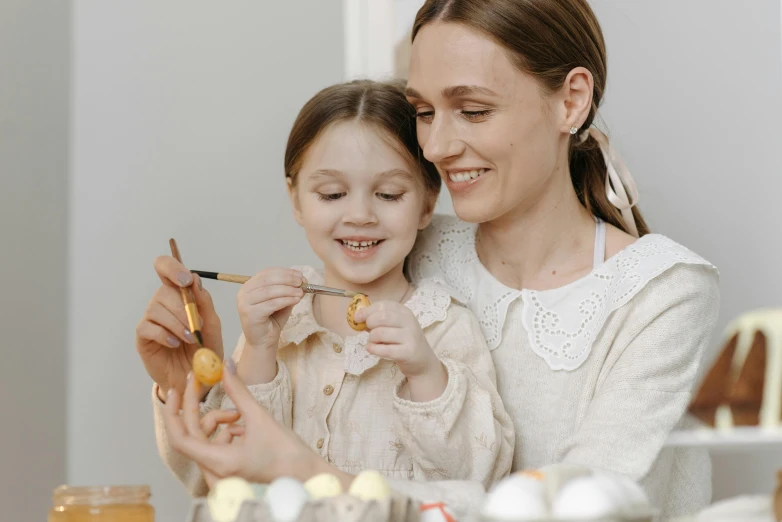 a woman and a little girl are painting eggs, pexels contest winner, portrait image, brown and cream color scheme, miniatures, digital image