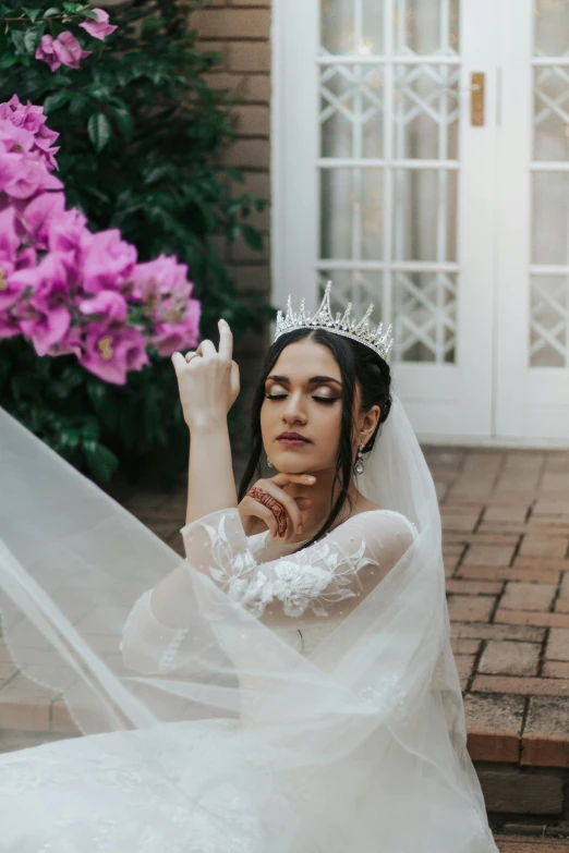 a woman in a wedding dress sitting on the ground, intricate flower tiara, hand on her chin, lush surroundings, sleek