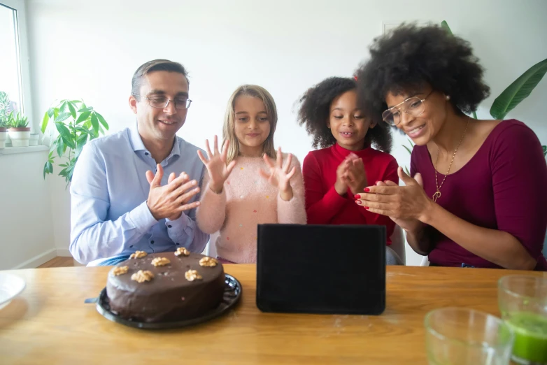 a group of people sitting around a table with a cake, in front of the internet