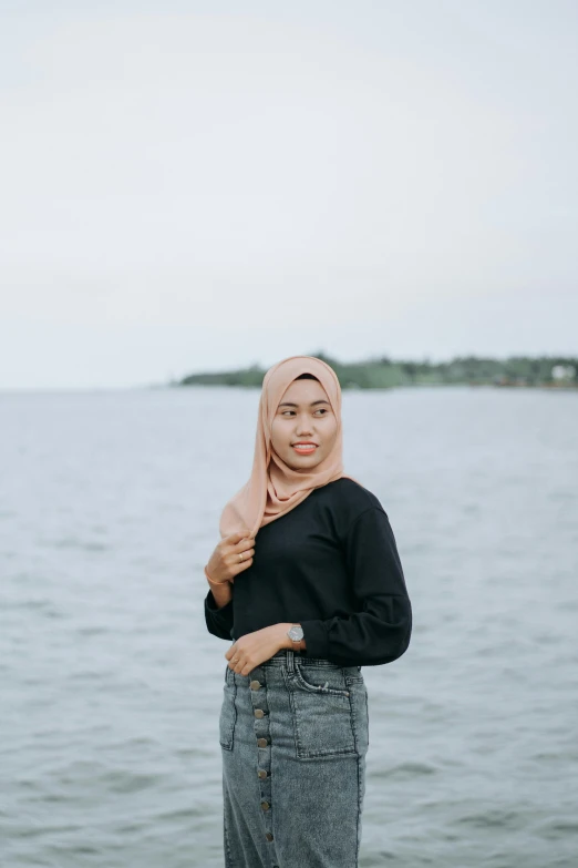 a woman standing in front of a body of water, a colorized photo, pexels contest winner, hurufiyya, wearing a black shirt, modest, young asian woman, smart casual