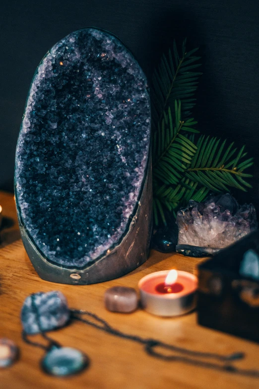 a candle sitting on top of a wooden table, a still life, by Julia Pishtar, trending on pexels, crystal cubism, amazing amethyst geode, 🌲🌌, dark glitter, displayed on an altar