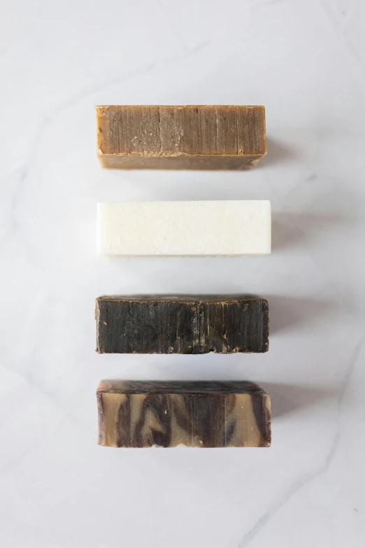 a group of soap bars sitting on top of a counter, by Jessie Algie, carbon black and antique gold, rustic wood, diverse textures, made of glazed