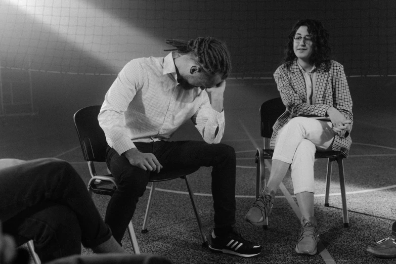 a black and white photo of two people sitting on chairs, a black and white photo, antipodeans, wearing adidas clothing, people crying, in meeting together, promotional image