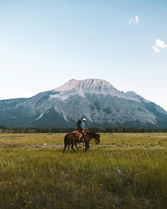 a man riding a horse across a lush green field, by Brigette Barrager, trending on unsplash, banff national park, icy mountains in the background, early evening, 🐎🍑