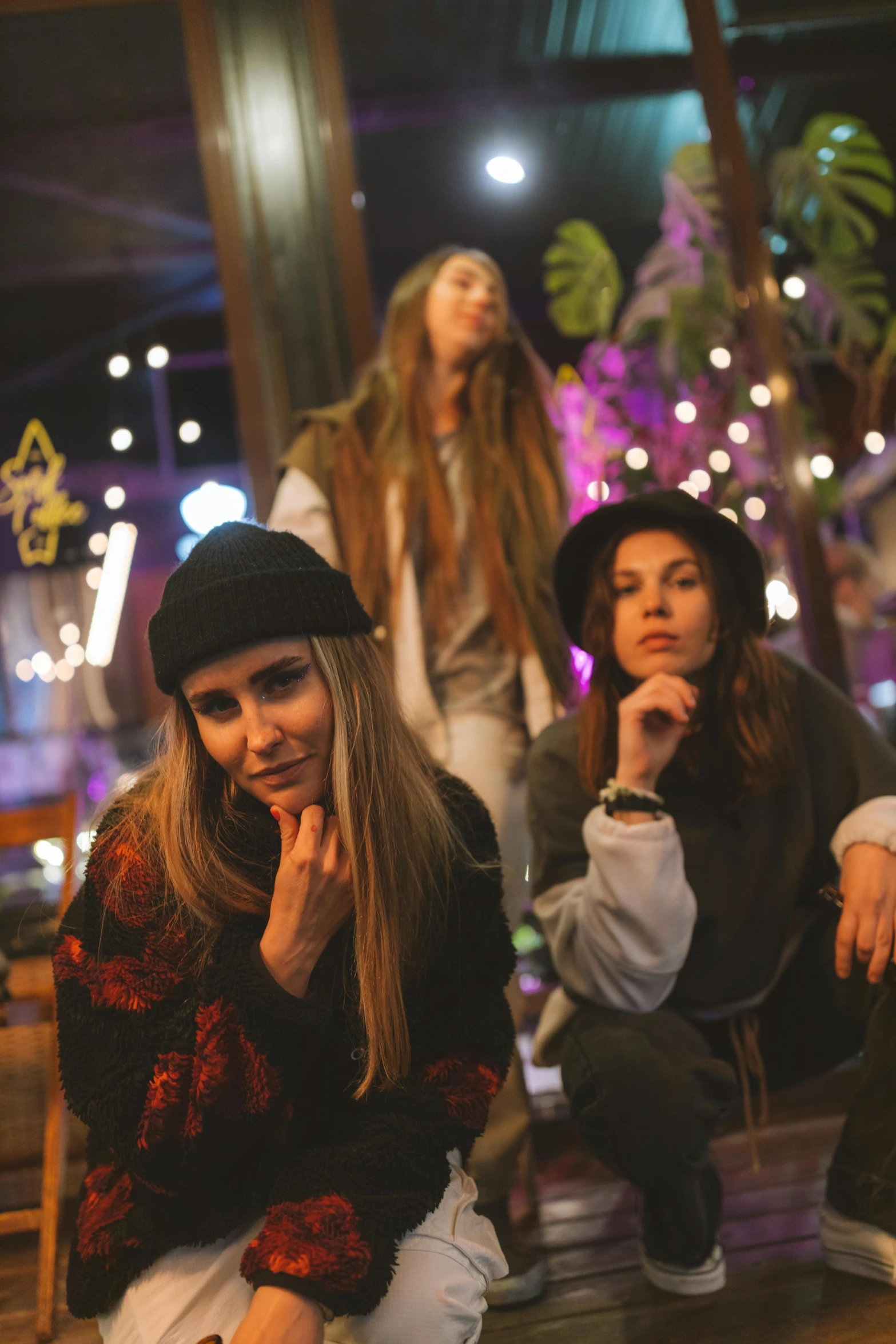 a group of women sitting on top of a wooden bench, an album cover, trending on pexels, antipodeans, wearing a beanie, night lights, portrait pose, three women