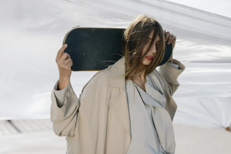 a woman holding a skateboard over her head, by Emma Andijewska, wearing a duster coat, portrait featured on unsplash, carrying a tray, disheveled