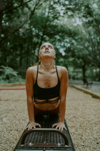 a woman in a black top doing a yoga pose, inspired by Elsa Bleda, pexels contest winner, at a park, young woman looking up, bench, wearing a vest top