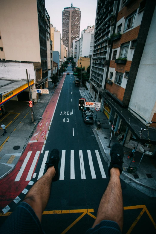 a man sitting on top of a street next to tall buildings, pexels contest winner, bird\'s eye view, futuristic sao paulo, legs taking your pov, standing bravely on the road
